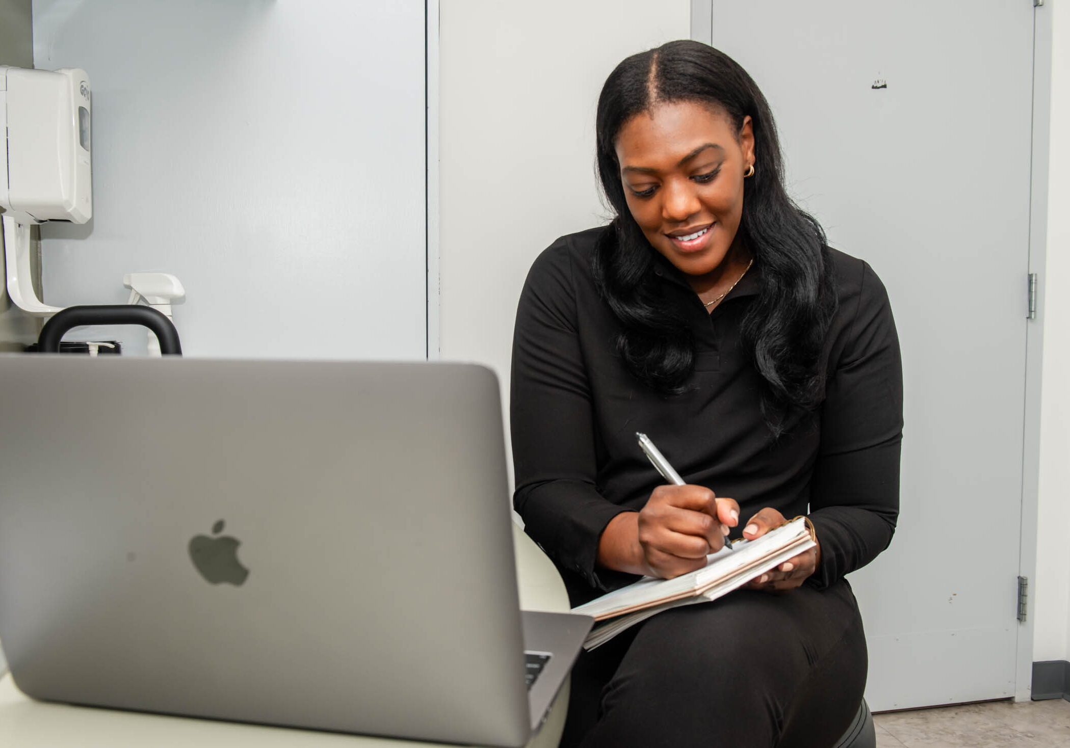 Woman writing notes beside a laptop.