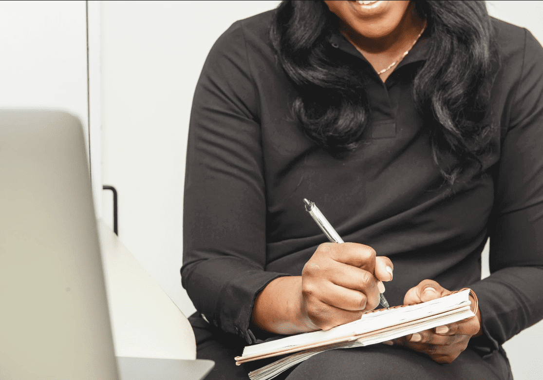 Person writing notes beside a laptop.